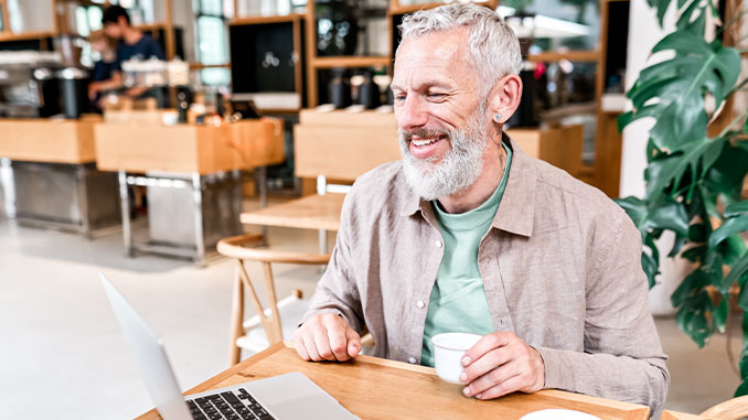 Ein Mann mittleren Alters sitzt fröhlich vor dem PC: Quereinstieg im Online Marketing
